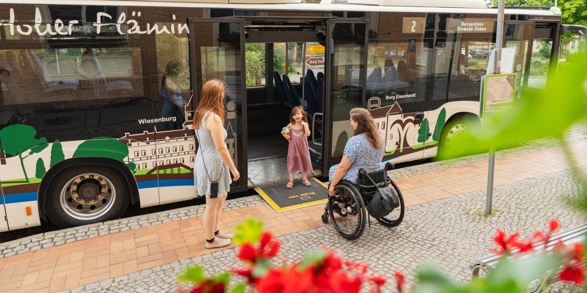 Ein Mädchen steht auf der Rollstuhlrampe eines Busses und wartet auf seine Mutter im Rollstuhl