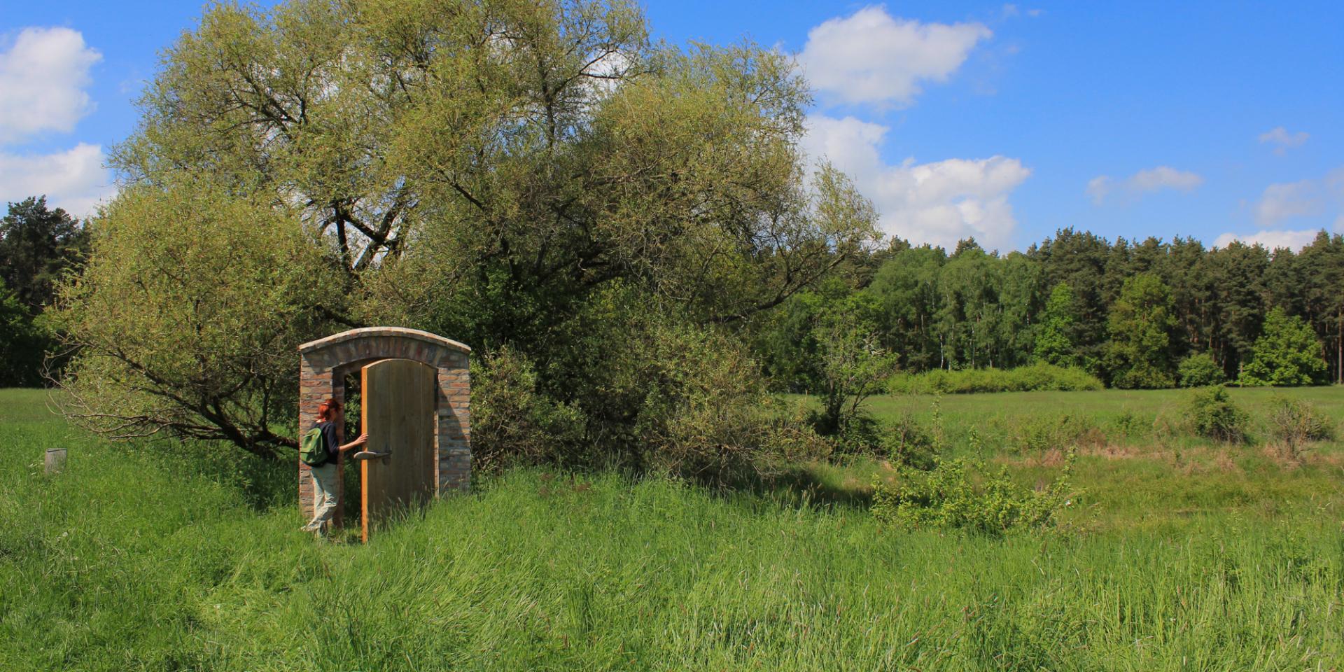 Eine Frau mit Rucksack geht durch eine Tür, die mitten in der Landschaft steht