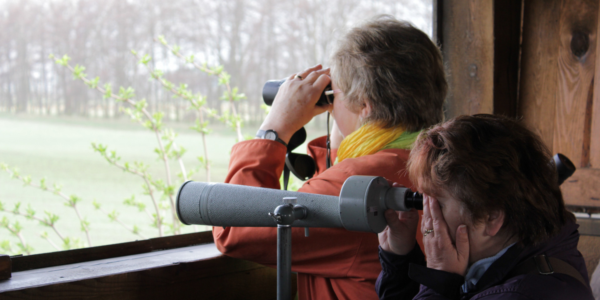 Zwei Frauen beobachten aus einer Schutzhütte durch Fernglas und Spektiv