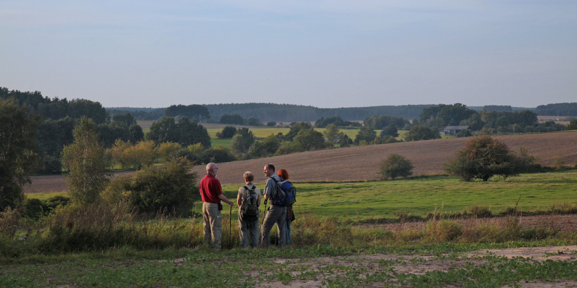 Eine Wandergruppe genießt die Aussicht in die Landschaft mit Feldern, Hecken und Gehölzinseln