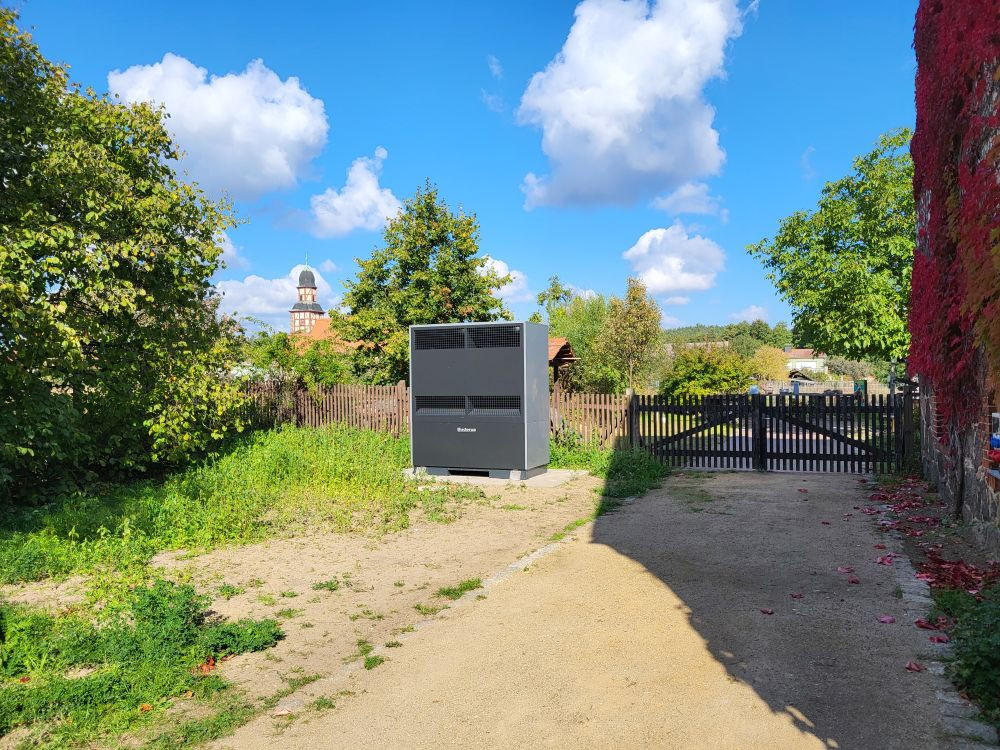 Ein grauer Kasten (die Wärmepumpe) mit Blick auf die Rabener Fachsteinkirche