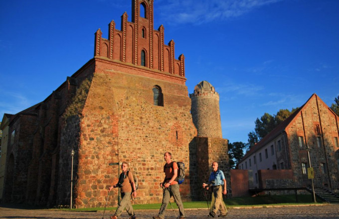 Eine Gruppe wandert vor einer Feldsteinwand mit rotem, gotisch anmutenden Backstein-Aufsatz
