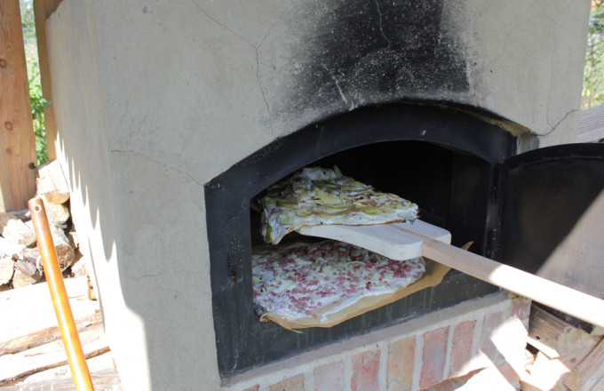 Ein Flammkuchen wird auf einem Holzschieber in den Lehmbackofen geschoben