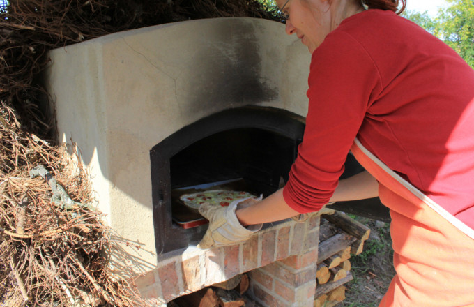 Eine Frau im roten Shirt schiebt ein Blech in einen Lehmbackofen