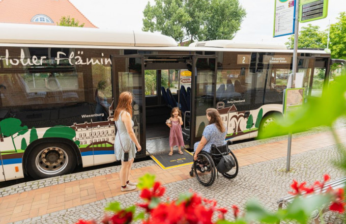 Ein Mädchen steht auf der Rollstuhlrampe eines Busses und wartet auf seine Mutter im Rollstuhl