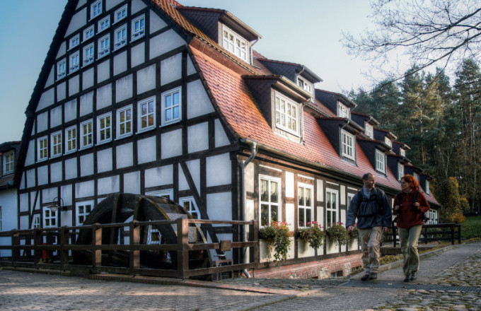 Ein Paar wandert an einer historischen Mühle mit Wasserrad, der Springbachmühle Bad Belzig, entlang