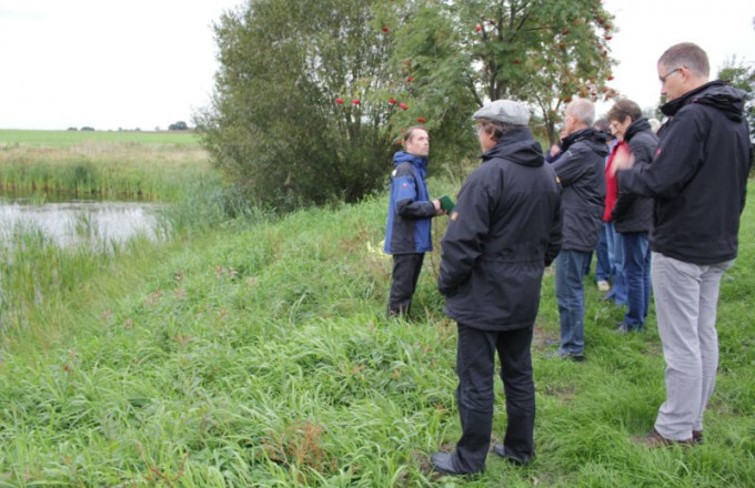 Eine Gruppe steht an einem Teich und hört einem Vortragenden zu
