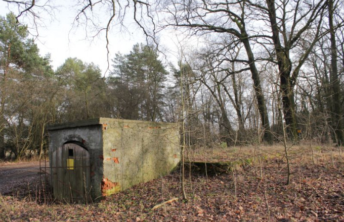 Blick auf einen Quaderbau, an dem der Putz abblättert und dessen Tür mit gelbem Schild durch ein Gitter gesichert ist