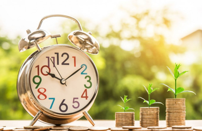 Ein Wecker steht neben Töpfen, in denen etwas Grünes heranwächst