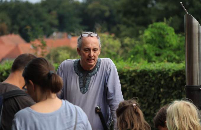 Ein violett gewandeter Mann spricht zu einer Gruppe