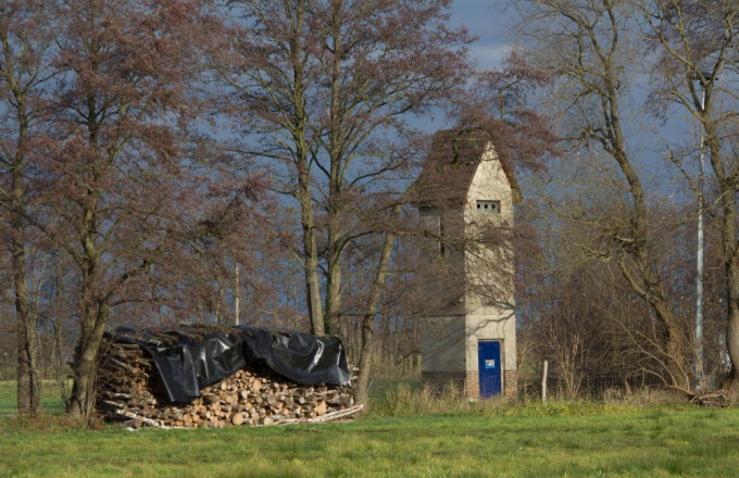 Steinturm unter Bäumen neben einem Holzstapel mit schwarzer Abdeckung