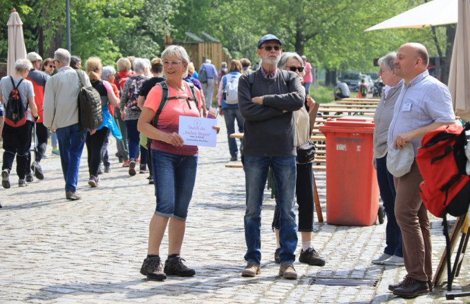 Eine Frau wartet mit einem Schild auf ihre Wandergruppe