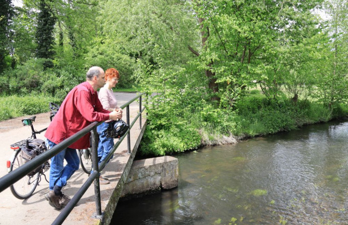 Ein Paar lehnt mit Fahrrädern am Brückengeländer und schaut in einen Bach