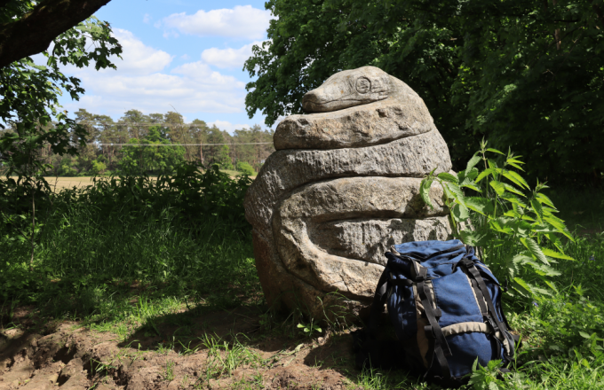 Ein Rucksack lehnt an einer Steinschlange