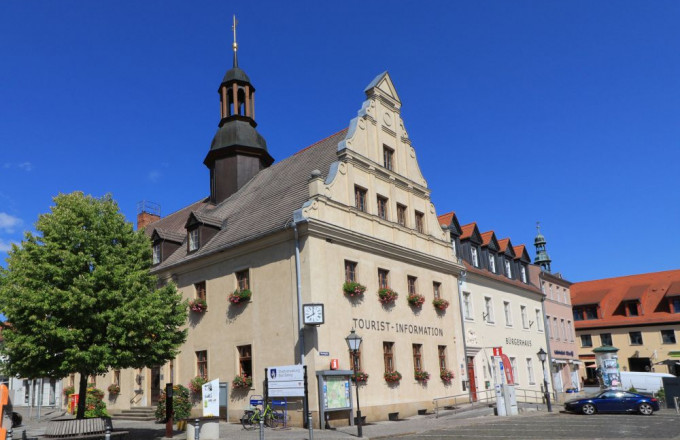 Cremefarbener Rathausgiebel mit dunklem Turm vor blauem Himmel