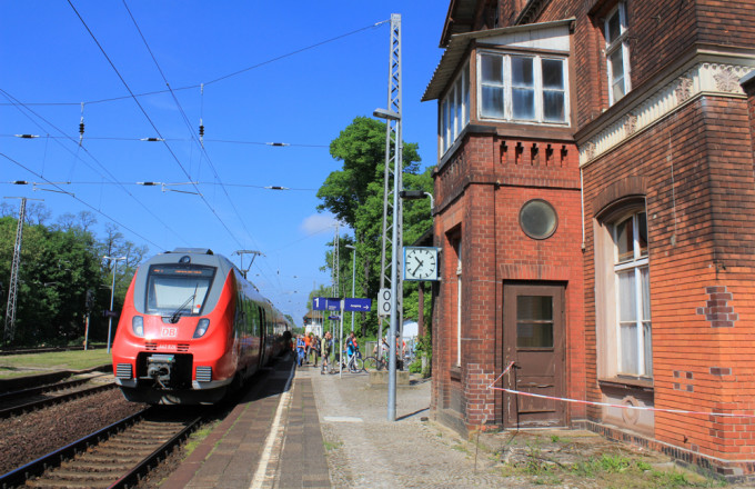 Ein Zug steht nebem dem Bahnhofsgebäude aus rotem Backstein
