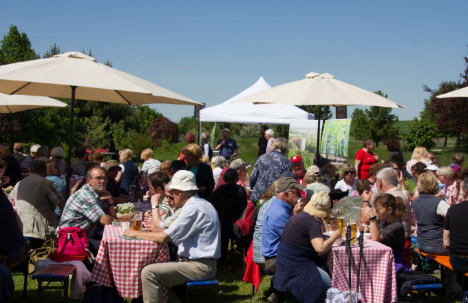 Viele Menschen sitzen an Tischen unter Sonnenschirmen.