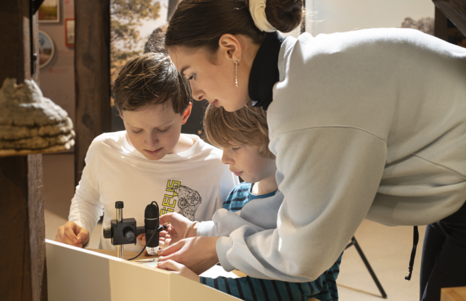 Eine Frau hilft zwei Kindern beim Mikroskopieren