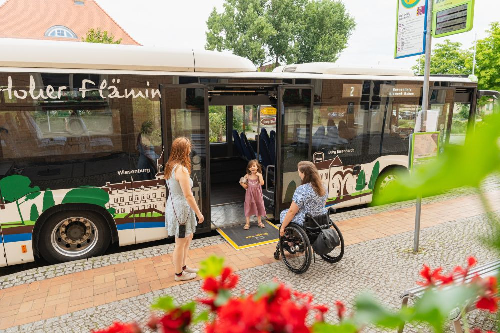 Ein Mädchen steht auf der Rollstuhlrampe eines Busses und wartet auf seine Mutter im Rollstuhl